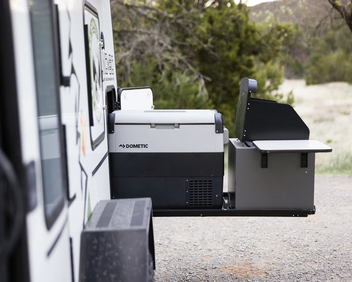 surrounded by nature.|This rugged No Boundaries off-road trailer rv rental with a rooftop tent and awning is perfectly set for adventure camping.|An RV rental's extended side compartment reveals a Dometic portable fridge and an outdoor grill station
