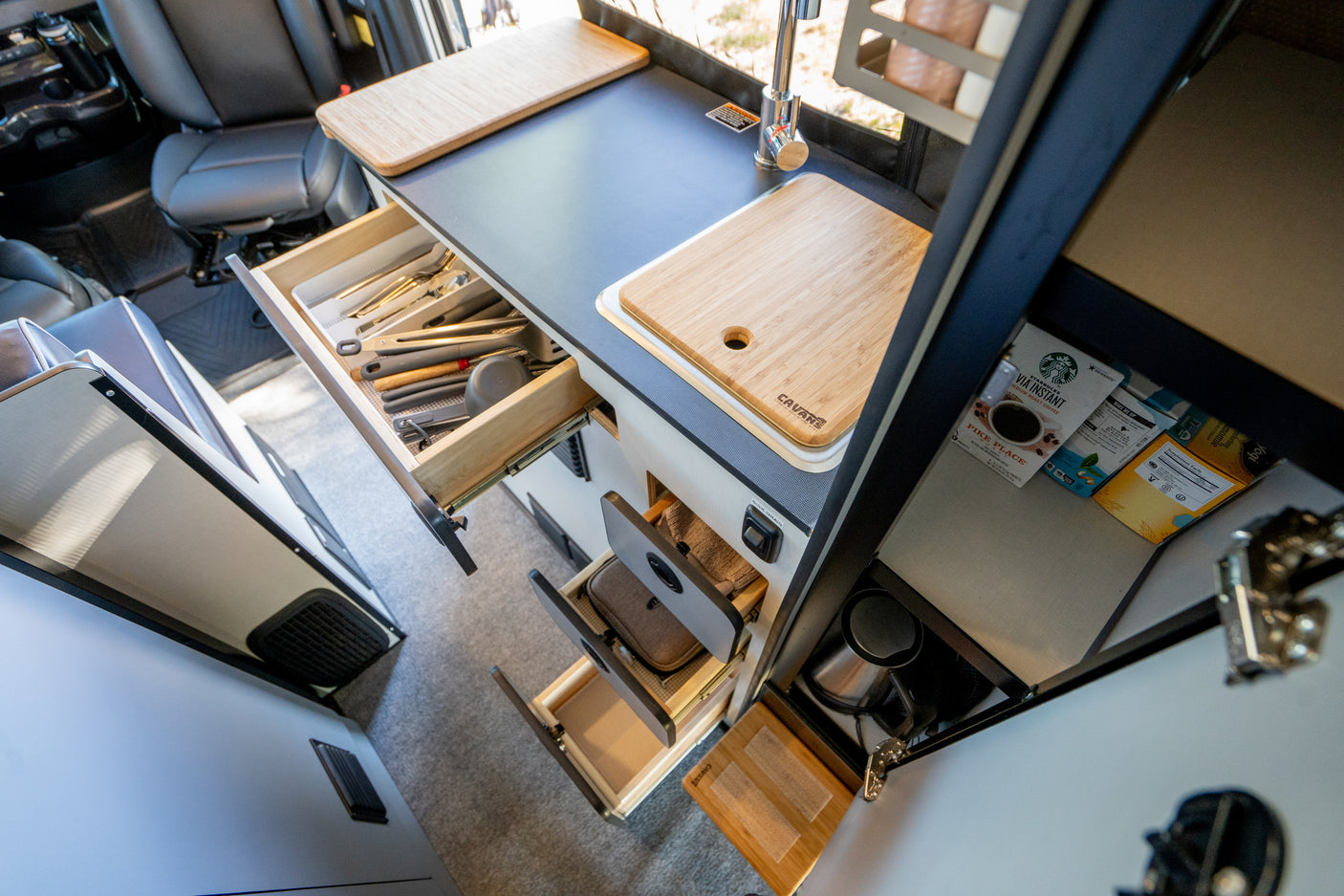 Functional RV rental kitchen with open drawers revealing organized utensils, sink, and coffee supplies.