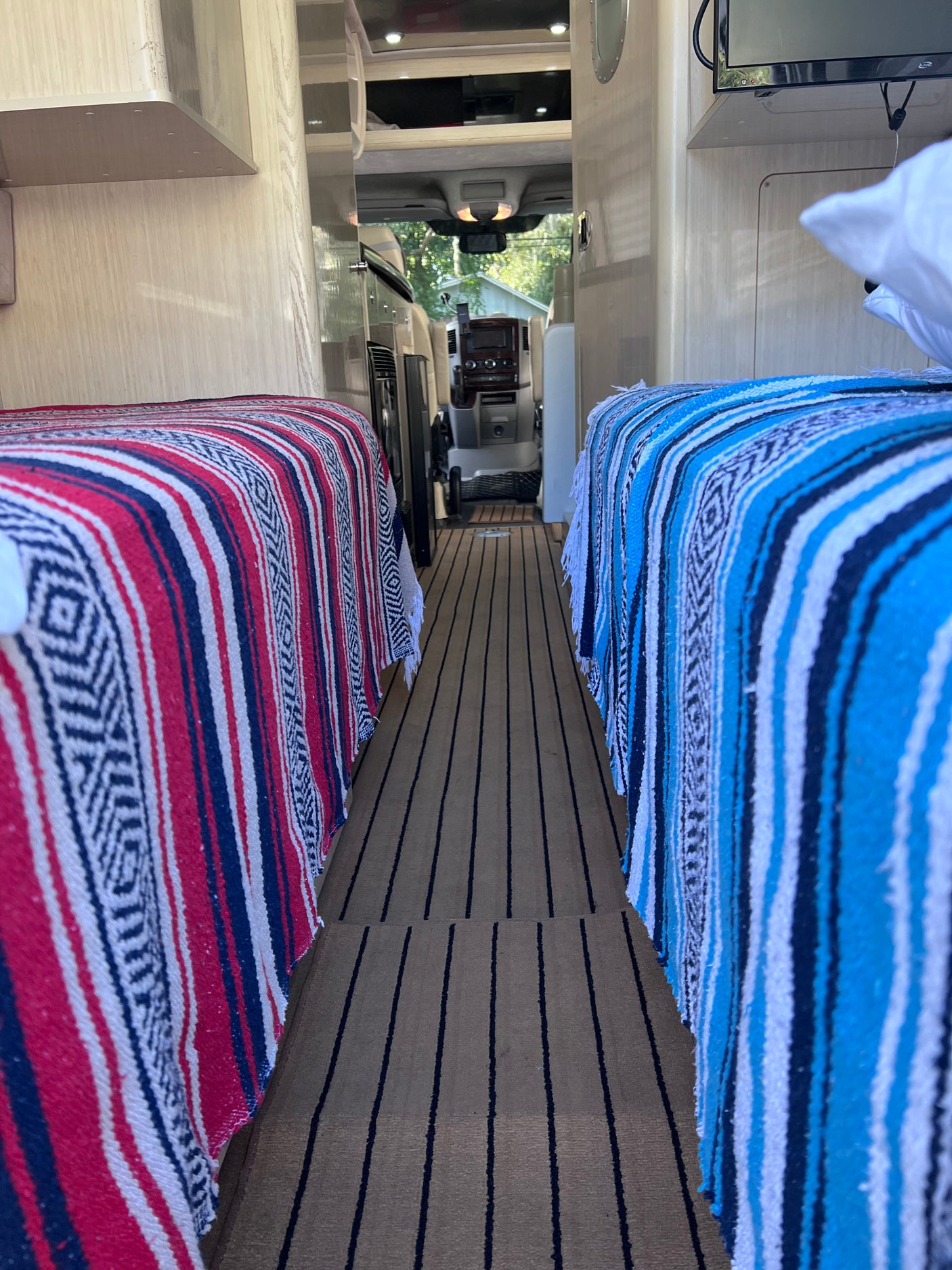 Cozy RV rental interior featuring two beds with patterned blankets & striped flooring, leading to the cockpit.