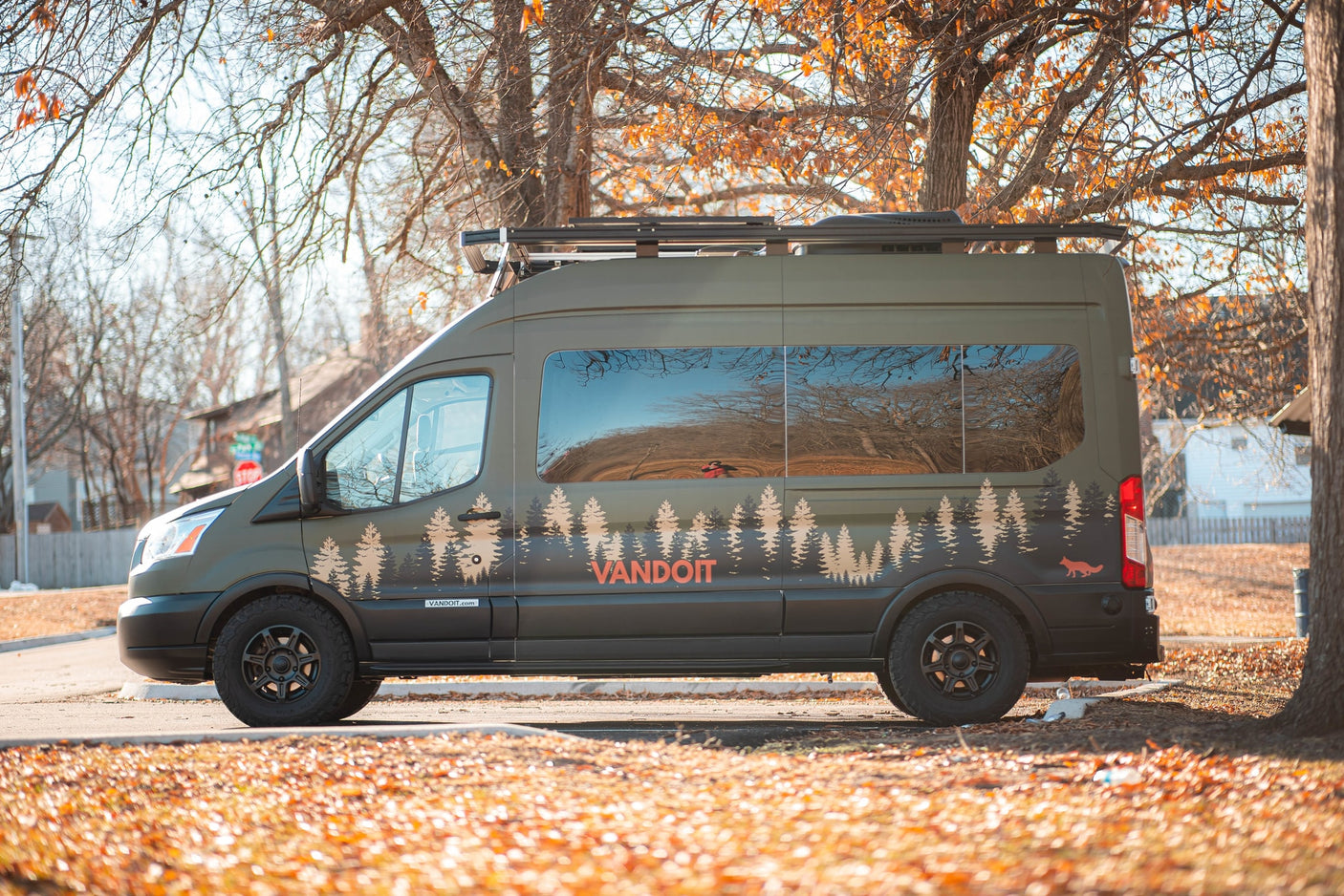 parked in an autumn setting.|Olive green Ford Transit camper van