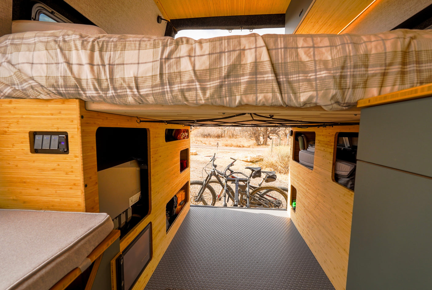 RV rental interior: elevated bed, bamboo storage, and mountain bikes at the rear, ready for outdoor adventures.