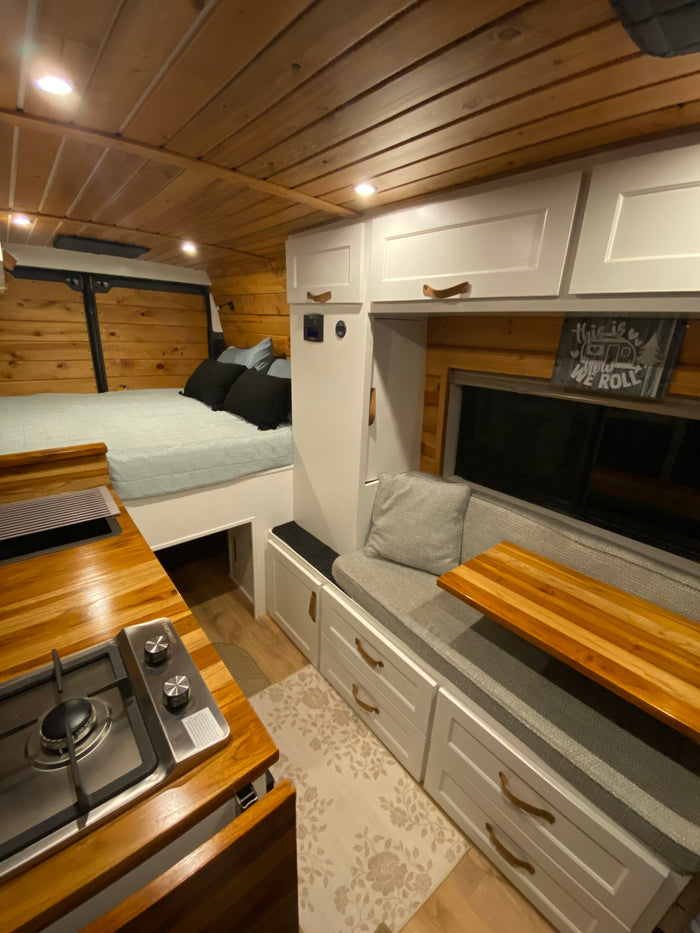 Inside a stylish RV rental: wood-paneled walls, a cozy bed, compact kitchen, and versatile seating.