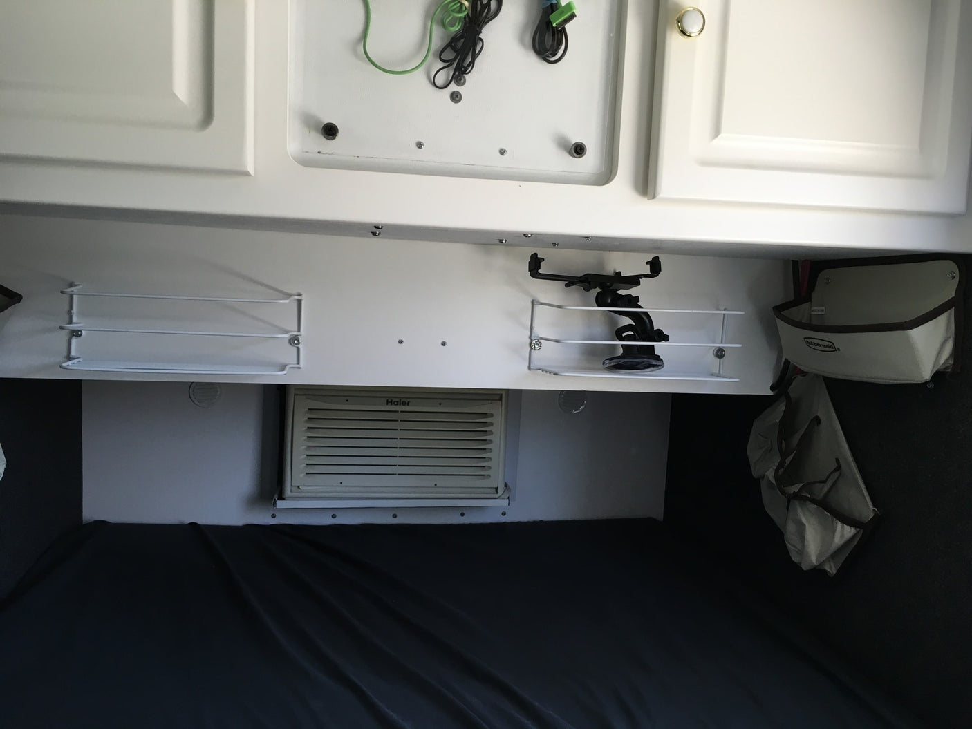 RV rental interior: white overhead cabinets, mounted shelves, a Haier AC unit, and a cozy bed area for travelers.