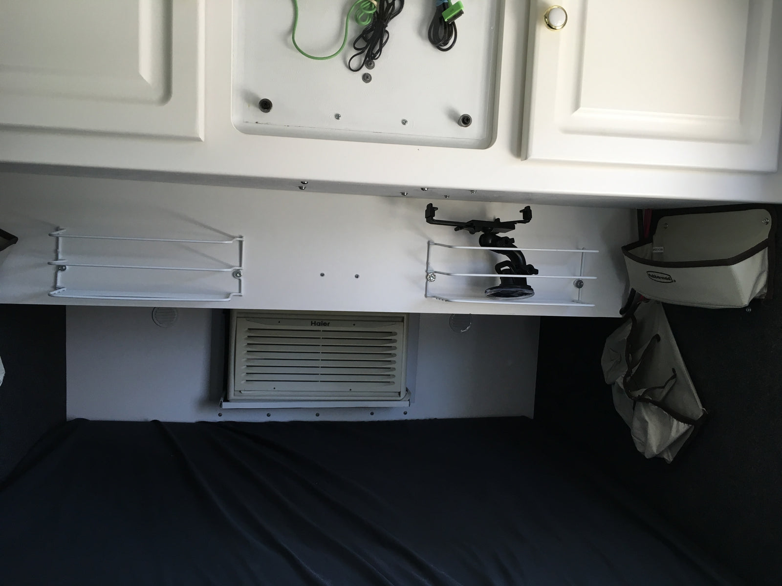 RV rental interior: white overhead cabinets, mounted shelves, a Haier AC unit, and a cozy bed area for travelers.