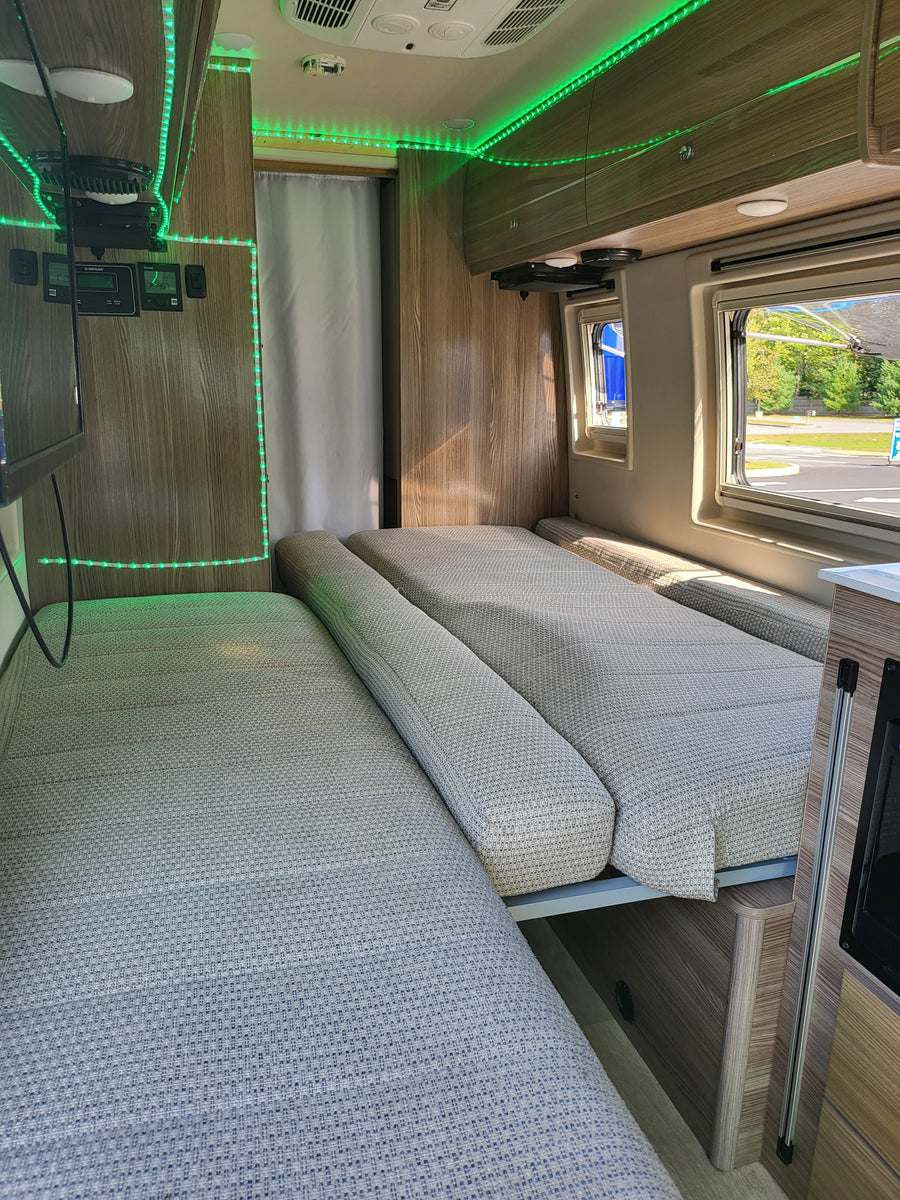Interior of an **RV rental** featuring two long padded beds/benches, accented by bright green LED strip lights and wood panels.