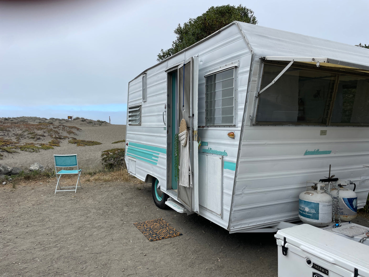 This vintage Land Commander RV rental offers a serene beachside escape, parked on sandy terrain under a cloudy sky.