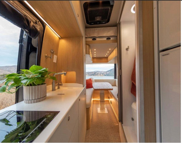 Explore this bright RV rental interior featuring a modern kitchen, cozy dining area, compact bathroom, and scenic outdoor views.