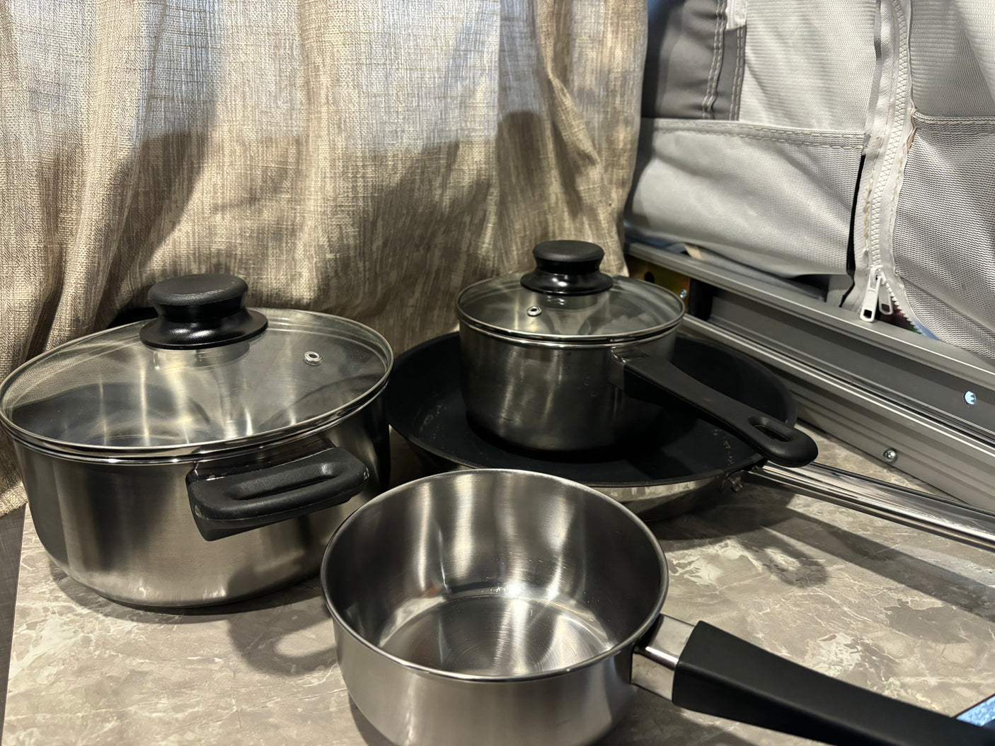 RV rental kitchenware: stainless steel pots, pans, and lids, ready for camping meals in a mobile kitchen.