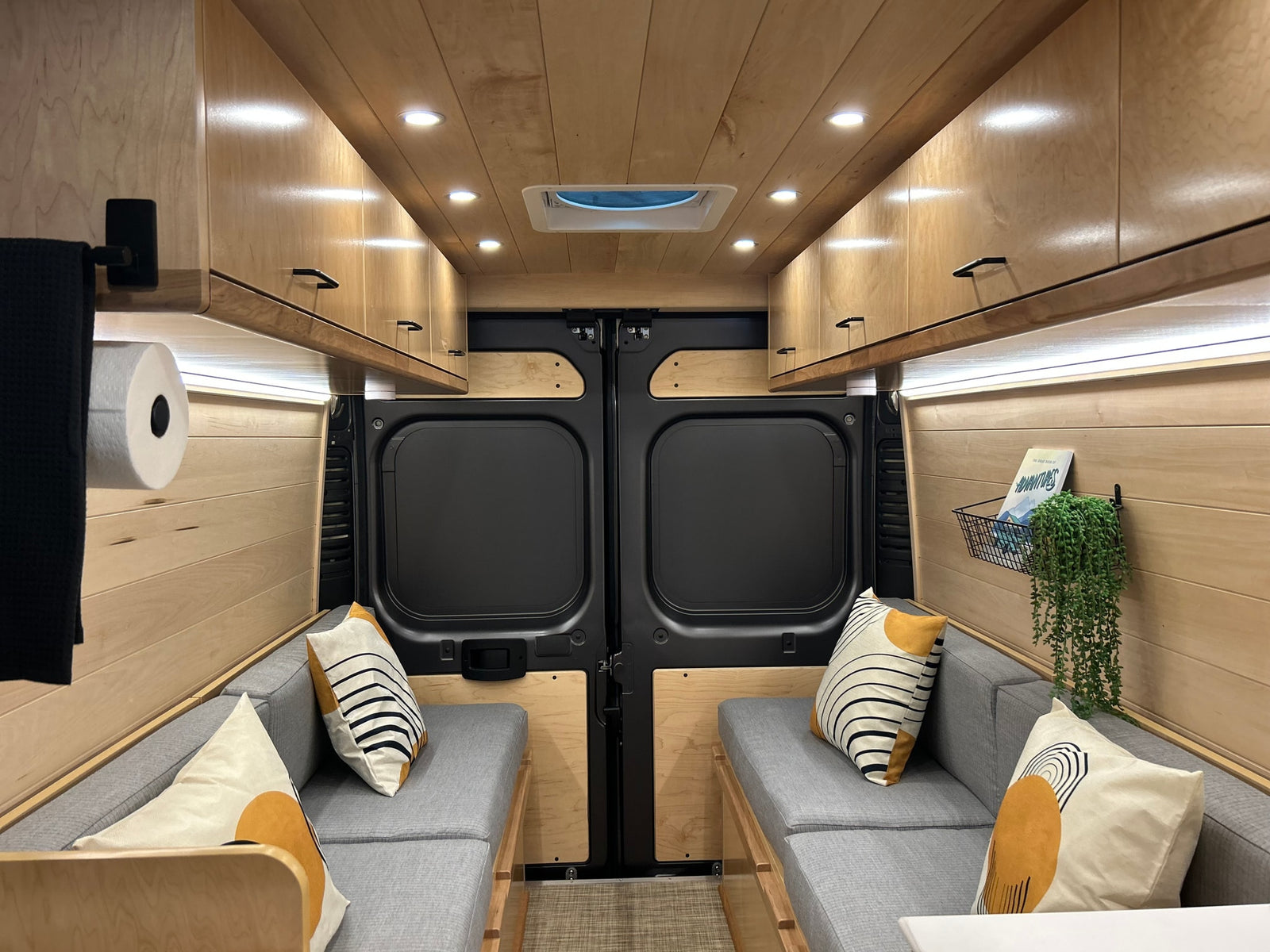 Cozy, modern camper van interior for your next RV rental adventure, featuring warm wood, comfy seating & smart storage.