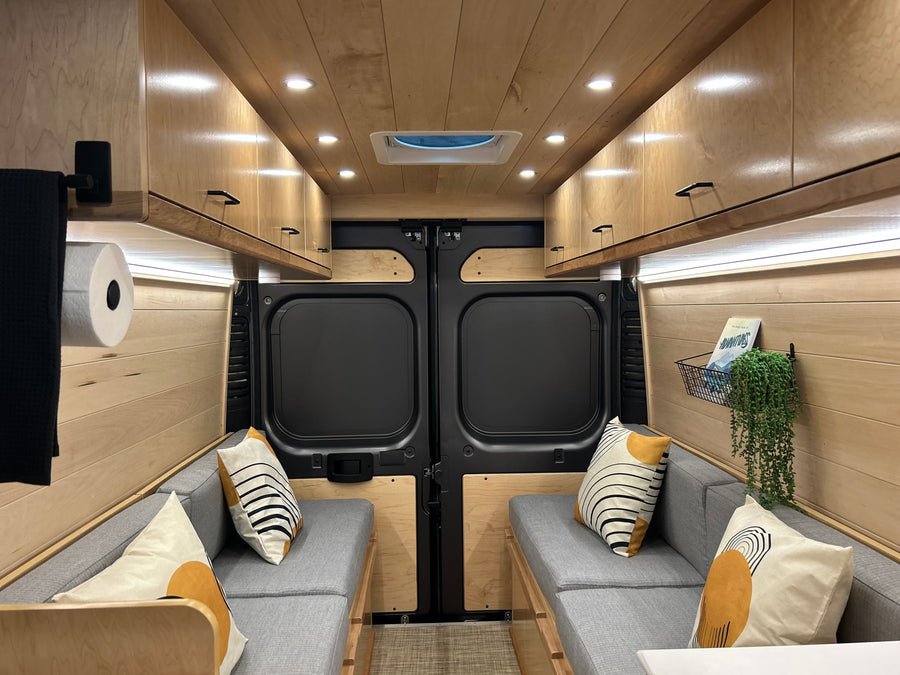 Cozy, modern camper van interior for your next RV rental adventure, featuring warm wood, comfy seating & smart storage.