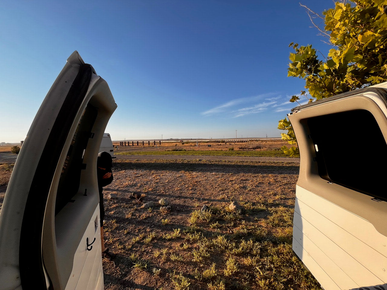 Your RV rental journey awaits! Open doors offer a wide view of a dry landscape, distant bridge, and clear sky.