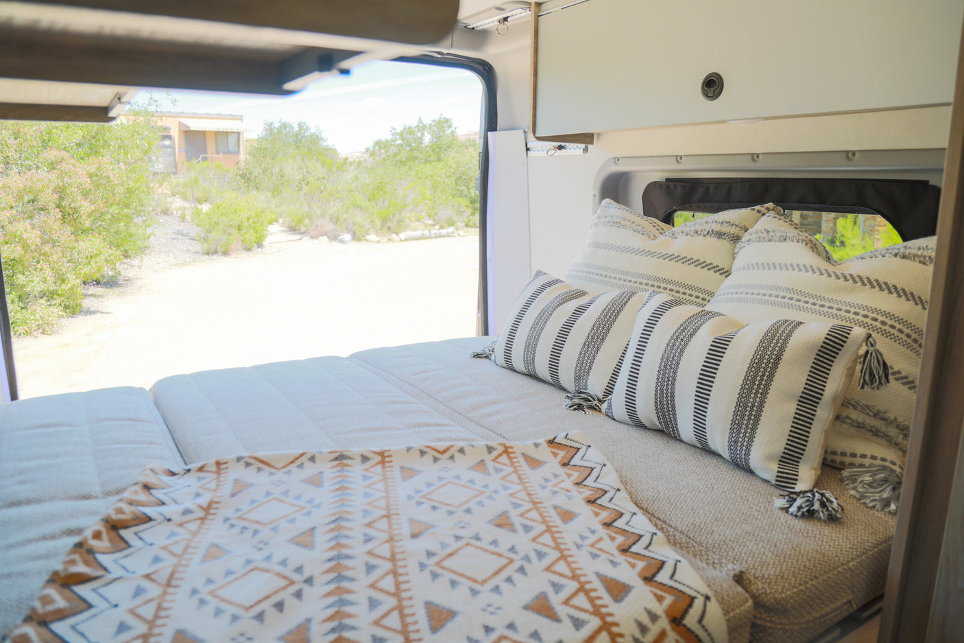 Inside an RV rental: a plush bed with patterned pillows and a clear view of the natural landscape.