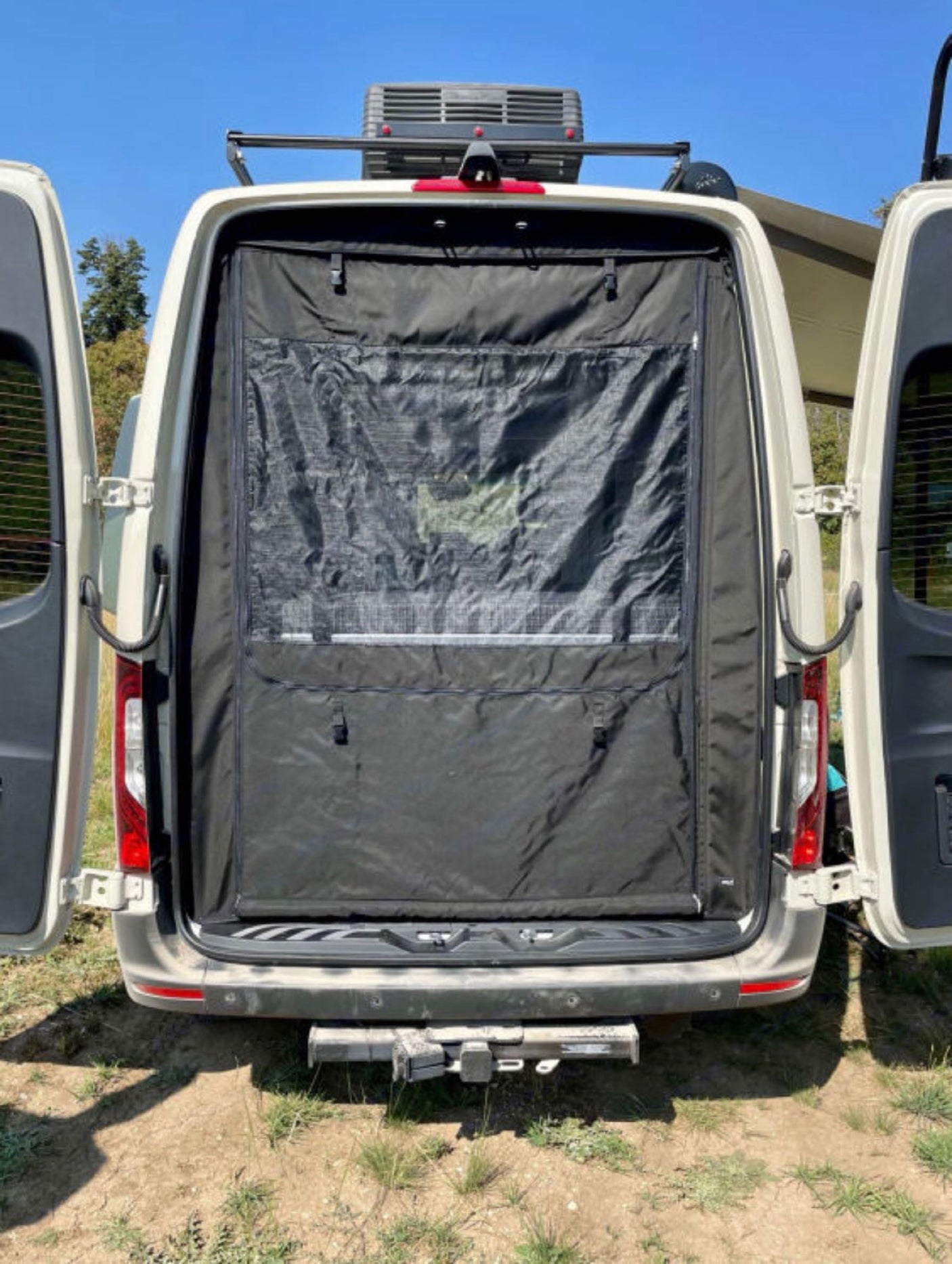 Rear of an RV rental camper van, doors open, showing a black privacy screen with mesh window, ready for adventure.