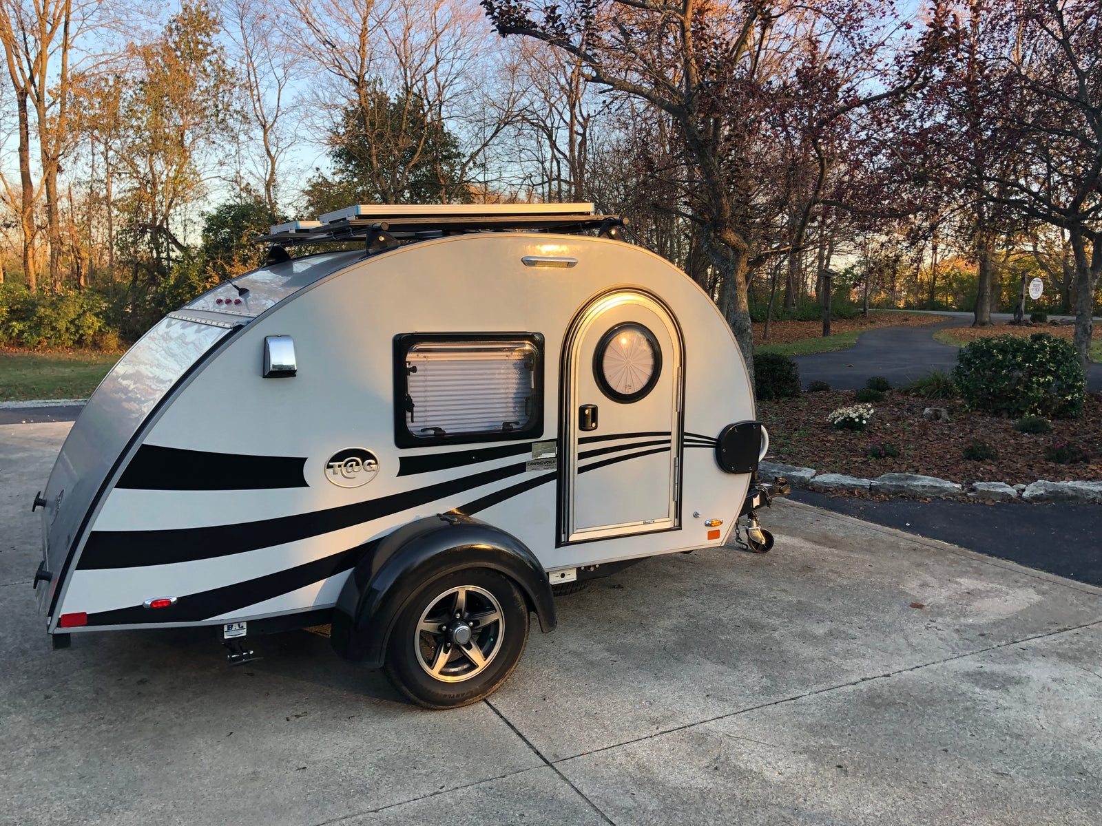 A stylish teardrop RV rental, grey with black stripes, parked on a driveway. Ready for camping adventures with solar power.