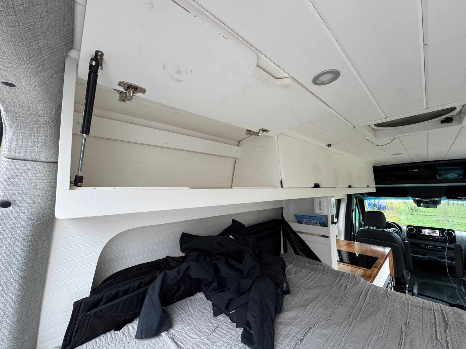 Cozy RV rental interior with bed & overhead storage. Front cab visible, perfect for travel.