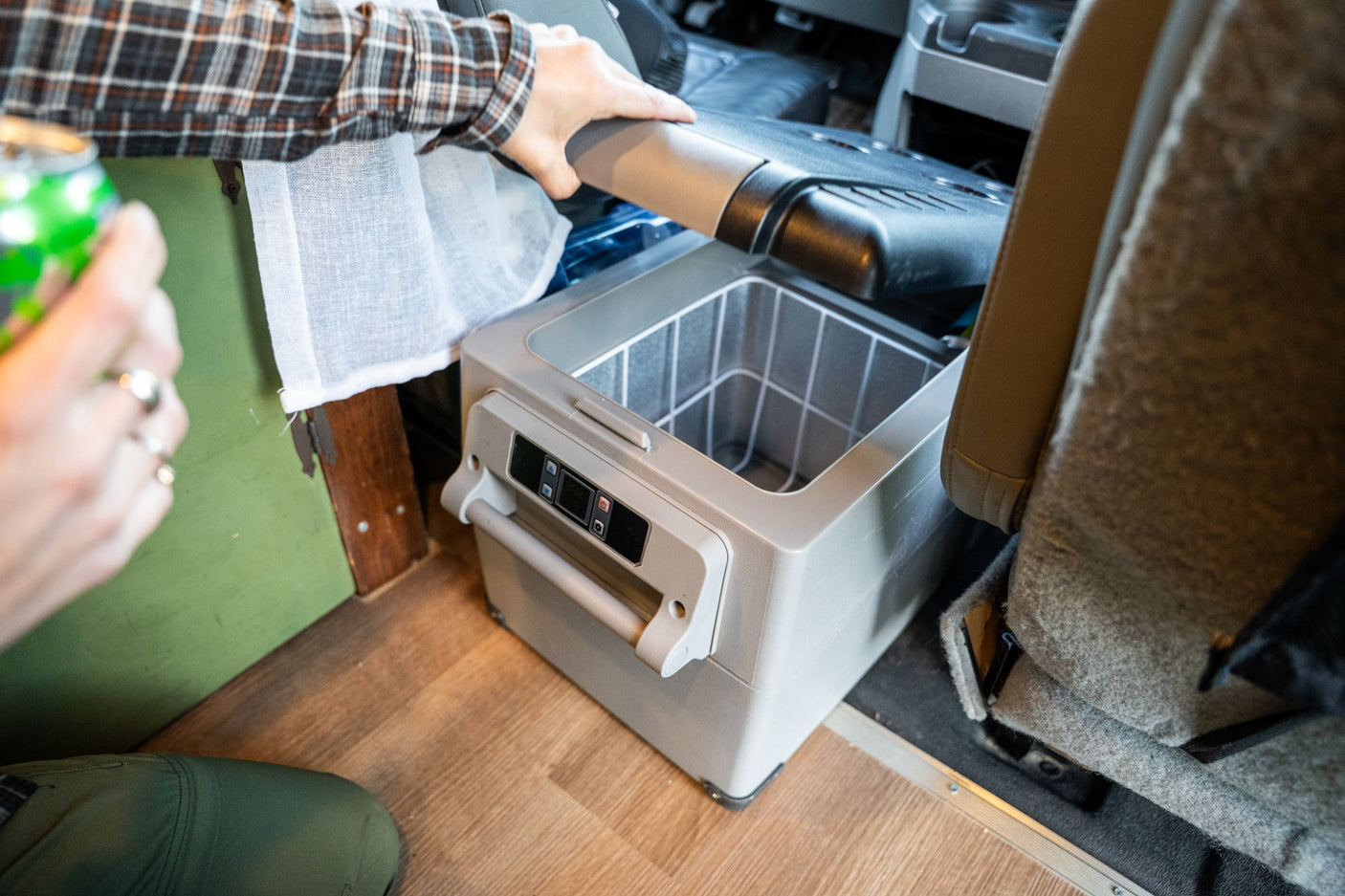An RV rental user opens a portable fridge inside their camper van, revealing a wire basket. Ideal for road trip drinks.
