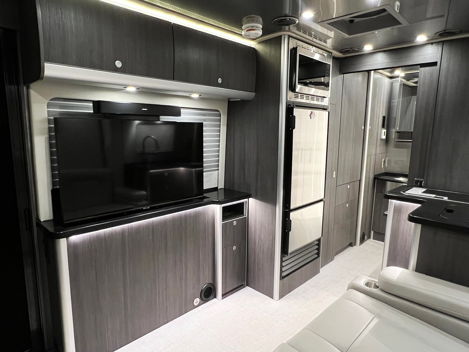 Explore this modern RV rental interior featuring a TV, Bose soundbar, microwave, fridge, and stylish storage.
