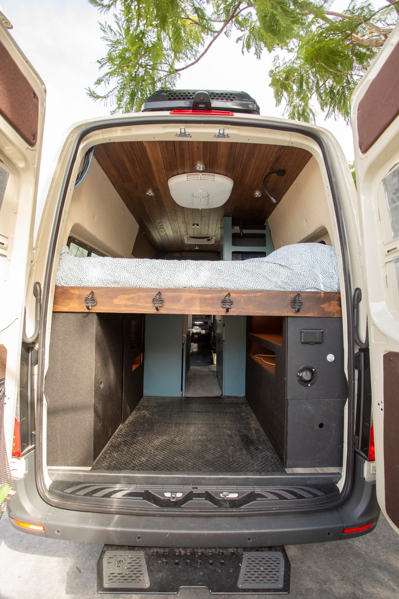 Inside this RV rental camper van: a cozy bed, ample storage, and custom wood paneling visible from the open rear doors. — photo 7