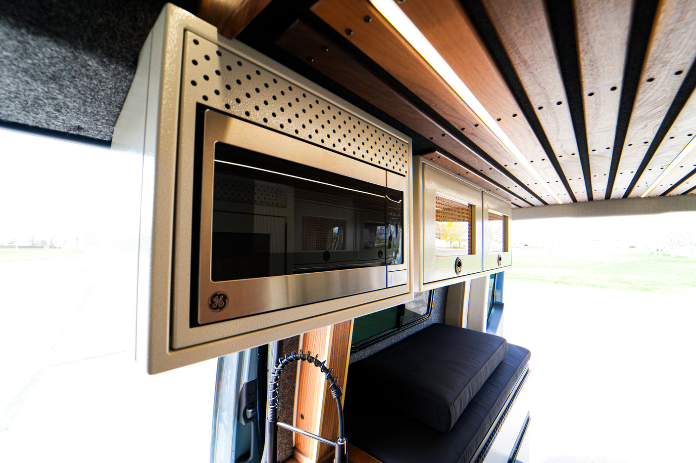 Inside an RV rental: a modern kitchen with a GE microwave, slatted ceiling, and cozy bench seating. Perfect for adventure.