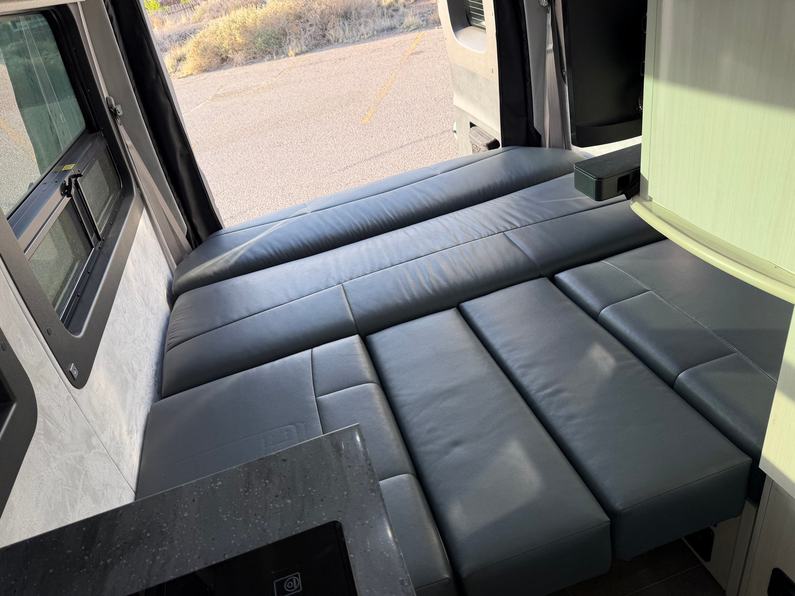 Modern rv rental: a versatile gray leatherette bed/seating area, outdoor window view, and integrated kitchen counter visible.