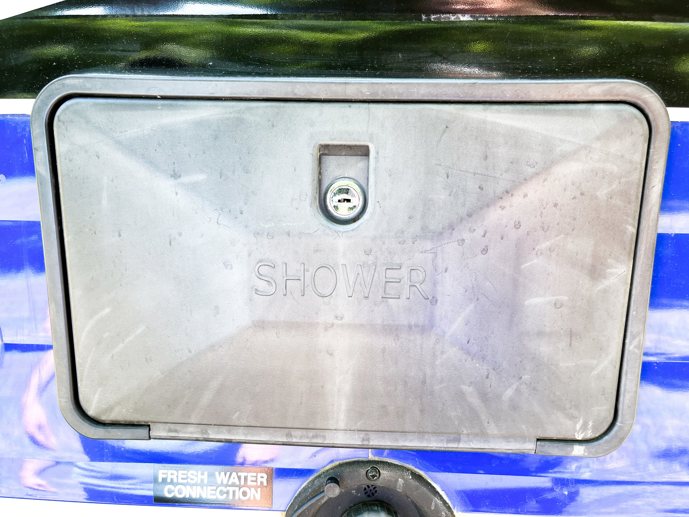 Outdoor shower and fresh water connection panel on an RV rental, featuring a lock and "SHOWER" embossed for outdoor use.