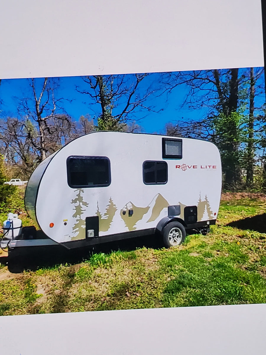 White RVE LITE teardrop RV rental featuring tree and mountain graphics, parked in a sunny outdoor setting.