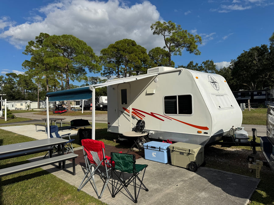 A white rv rental is parked at a sunny campsite with an awning