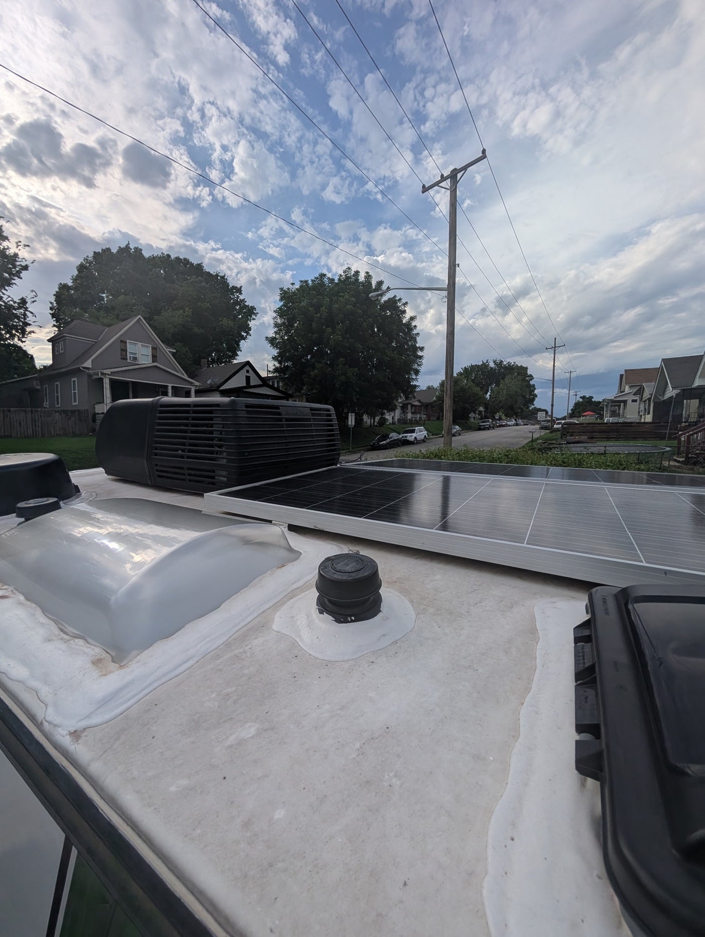 RV rental rooftop with solar panels, AC unit, and skylight, overlooking a residential street under a cloudy sky.