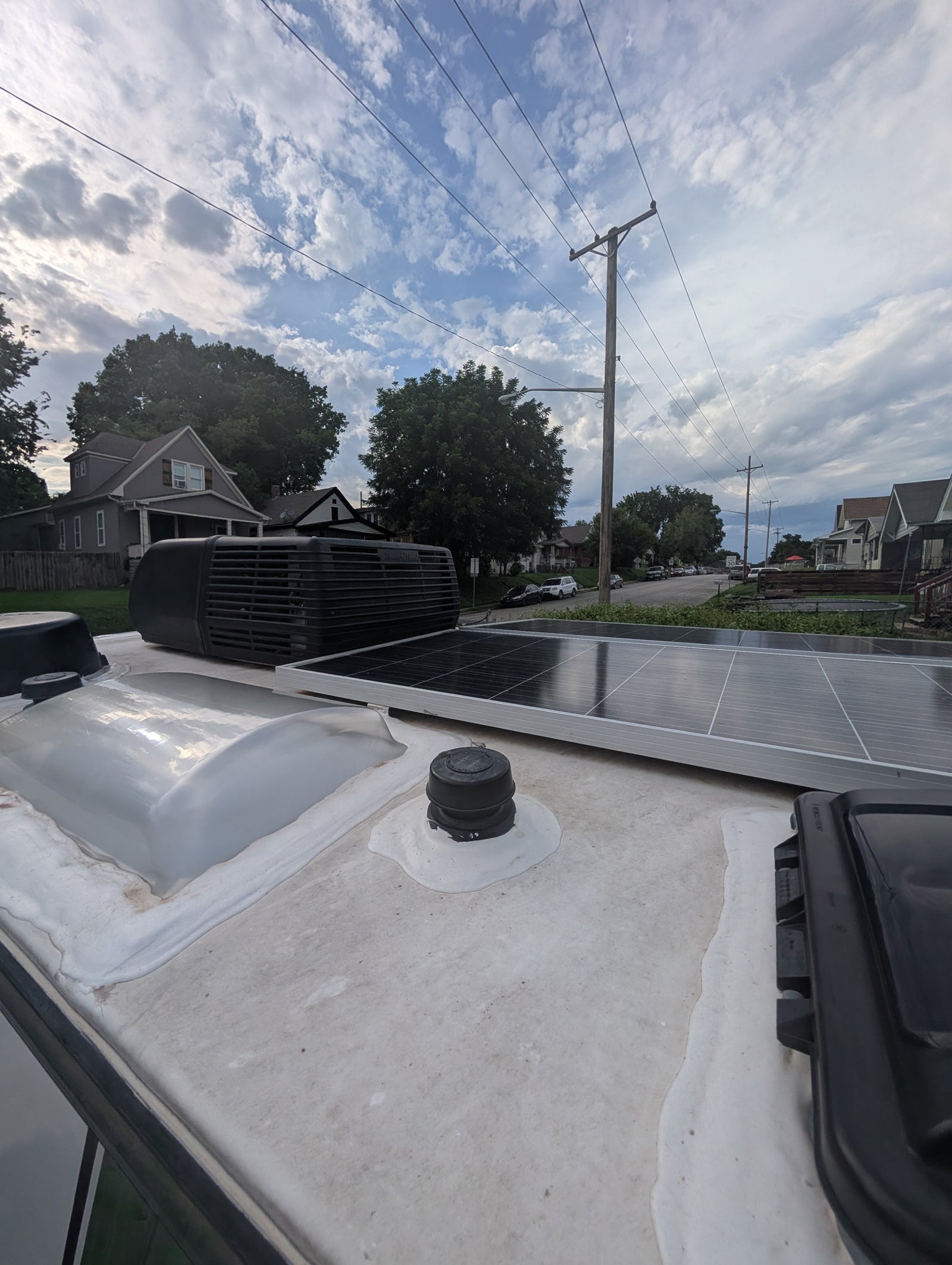 RV rental rooftop with solar panels, AC unit, and skylight, overlooking a residential street under a cloudy sky.