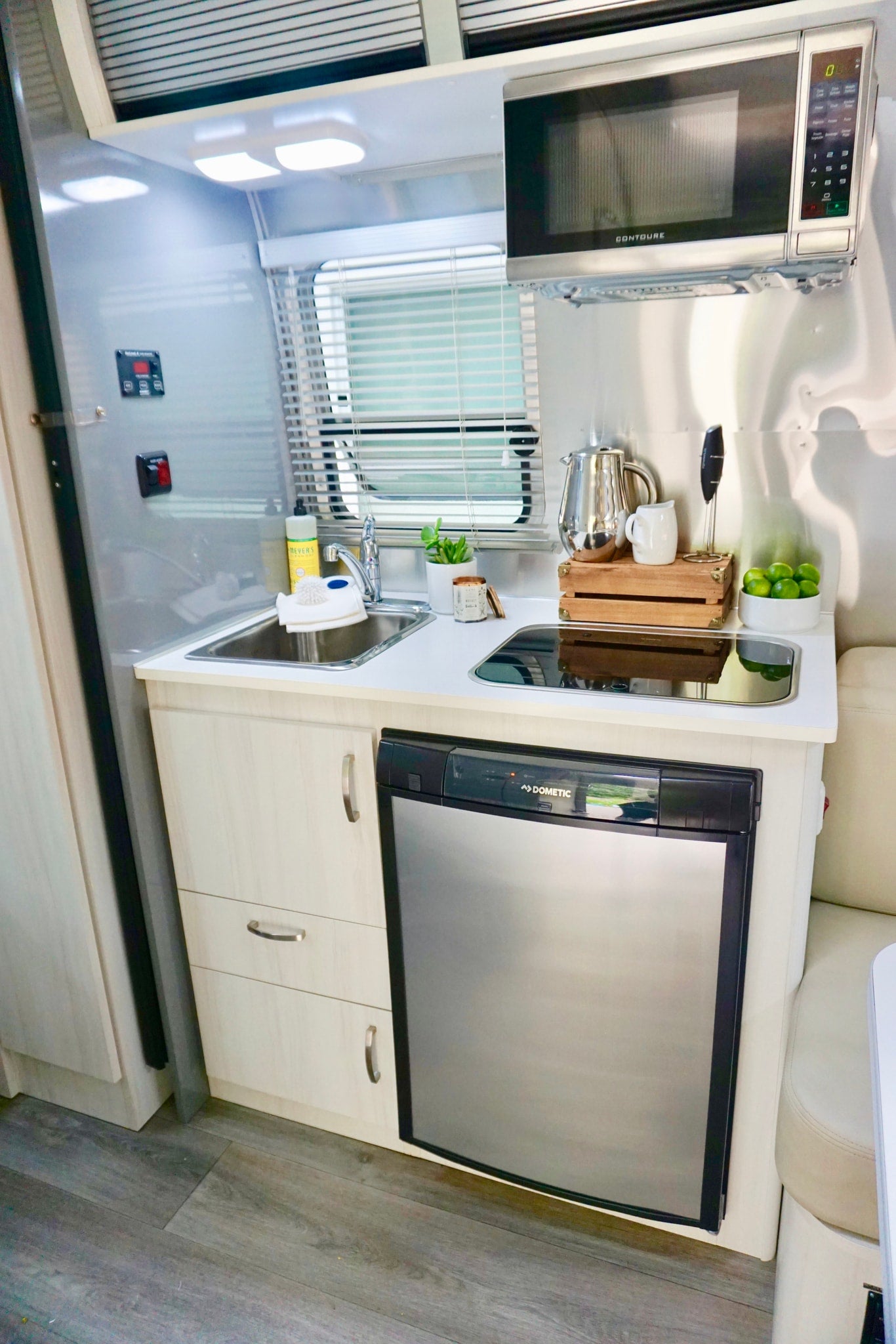 Compact rv rental kitchen: stainless steel walls, bright lights, Contoure microwave, sink, Dometic fridge, and wood floors. — photo 9