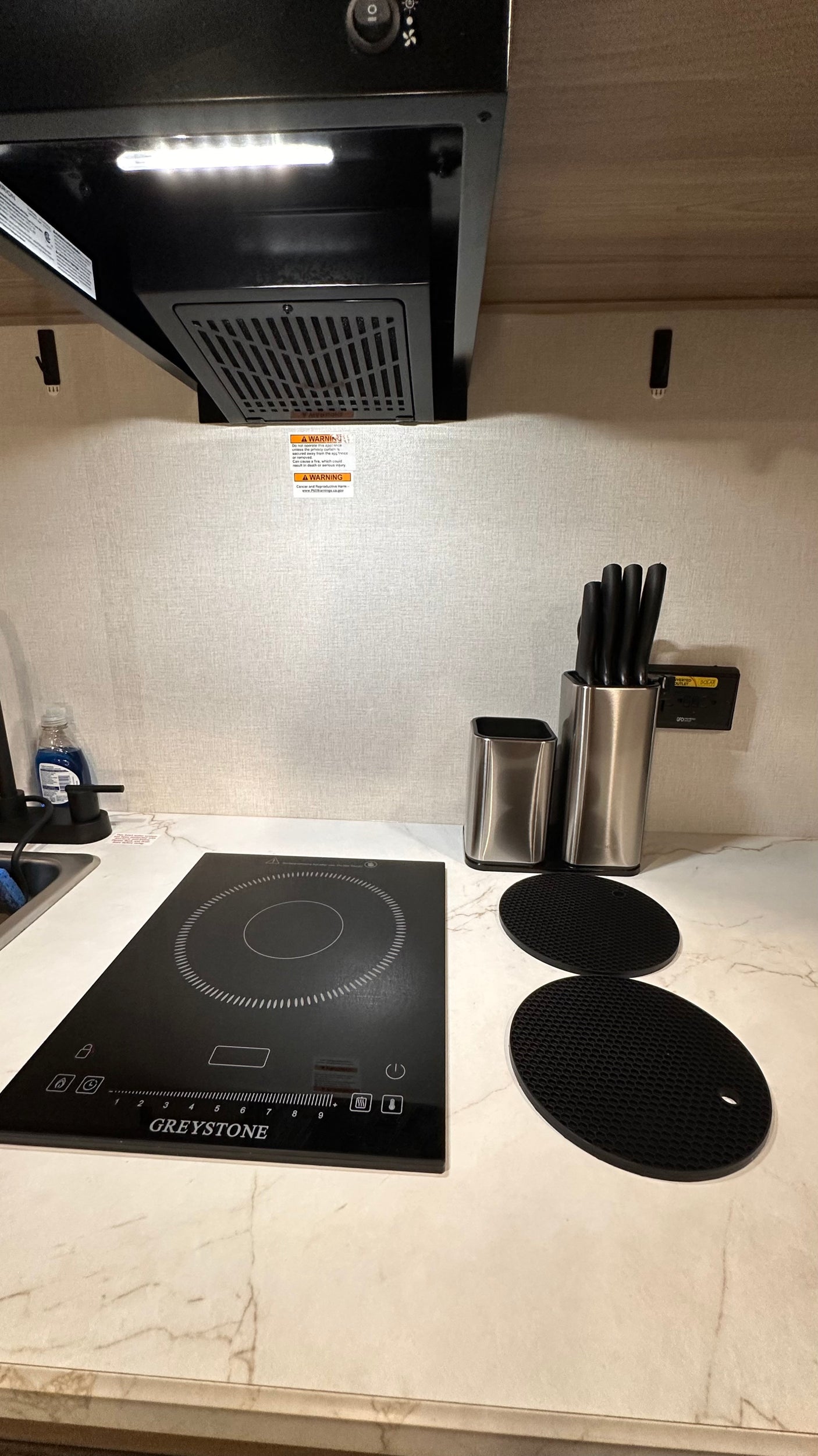 Compact rv rental kitchen with a Greystone induction cooktop, knife block, and range hood, perfect for travel cooking.