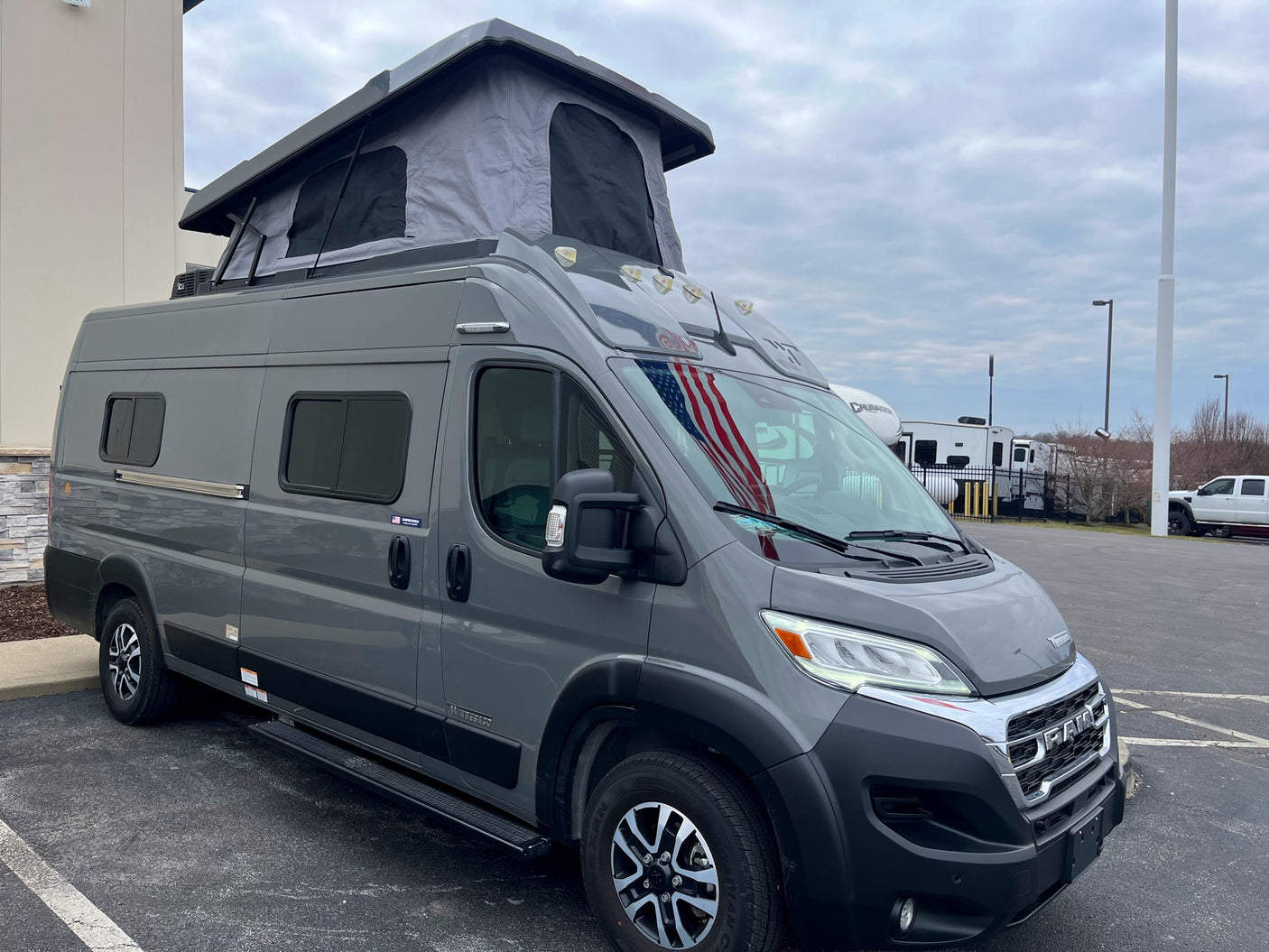 A gray Ram-based camper van with a raised pop-top roof, seen outdoors, ideal for an rv rental adventure.