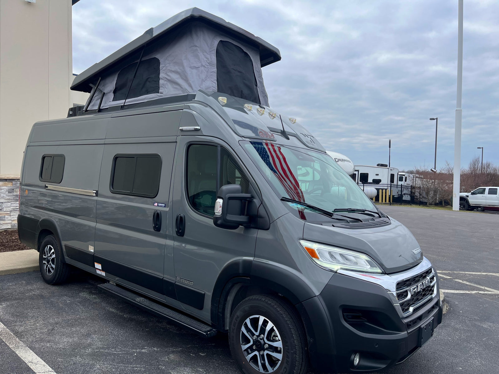 A gray Ram-based camper van with a raised pop-top roof, seen outdoors, ideal for an rv rental adventure.