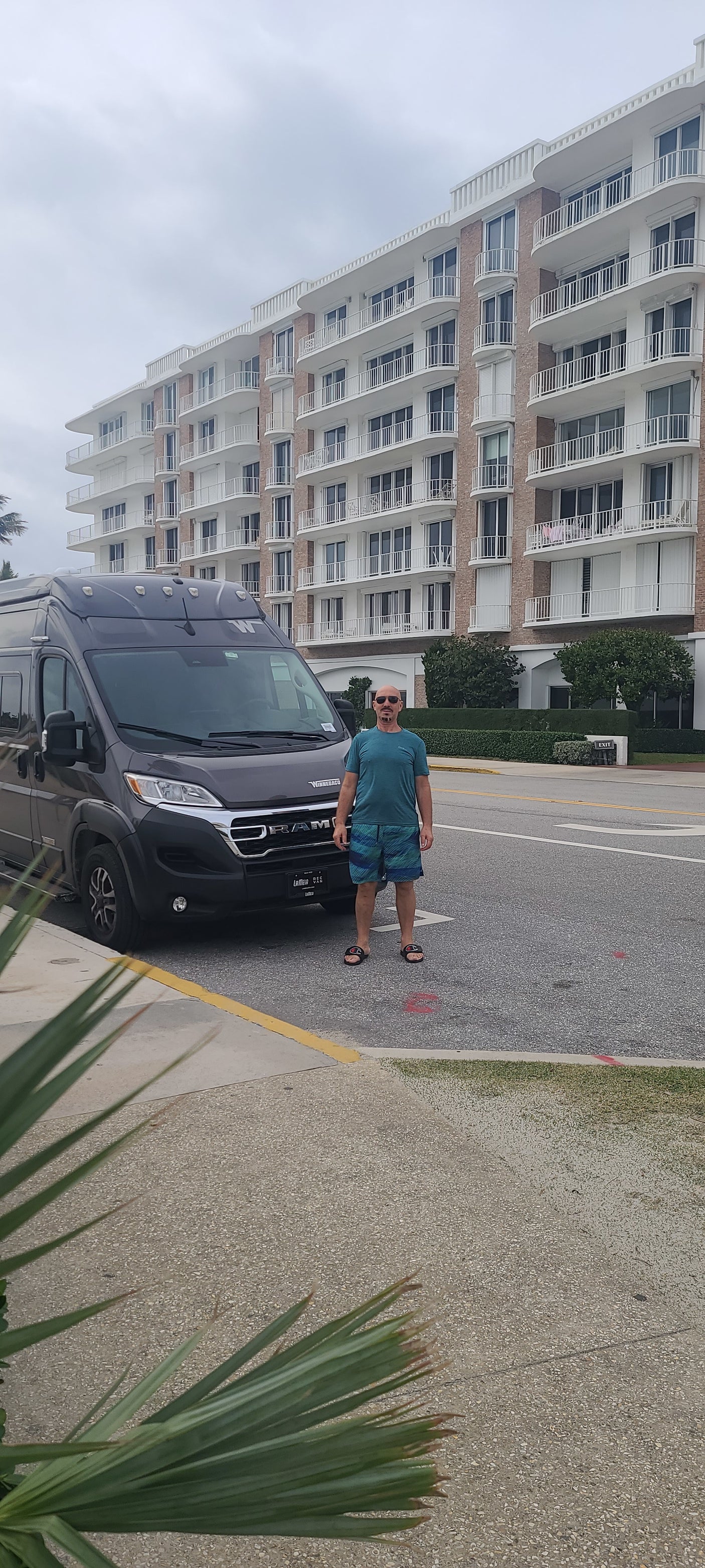 Man stands next to his gray RV rental van, a Winnebago, parked on a street in front of a grand building.