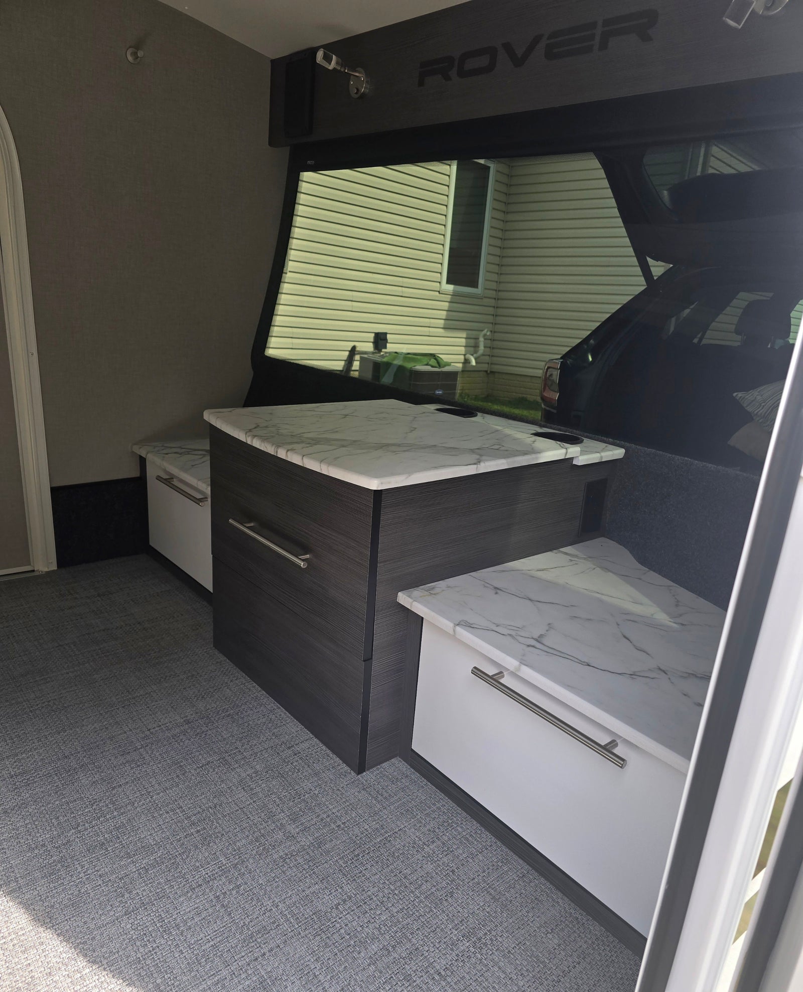 Explore this RV rental's modern interior: central dark cabinet with marble-look counter, side benches, and grey textured flooring.