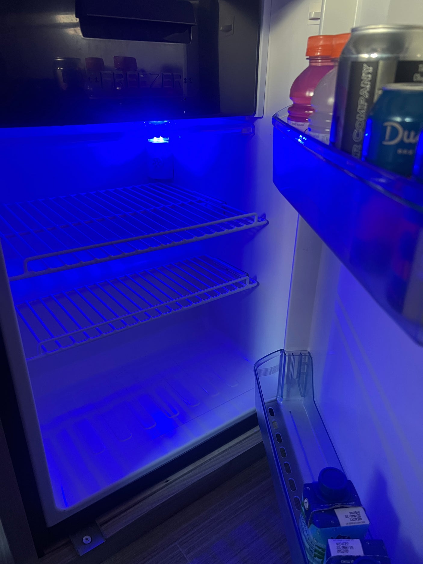 This RV rental mini-fridge, lit by a vibrant blue LED, offers compact storage for drinks and a small freezer section.