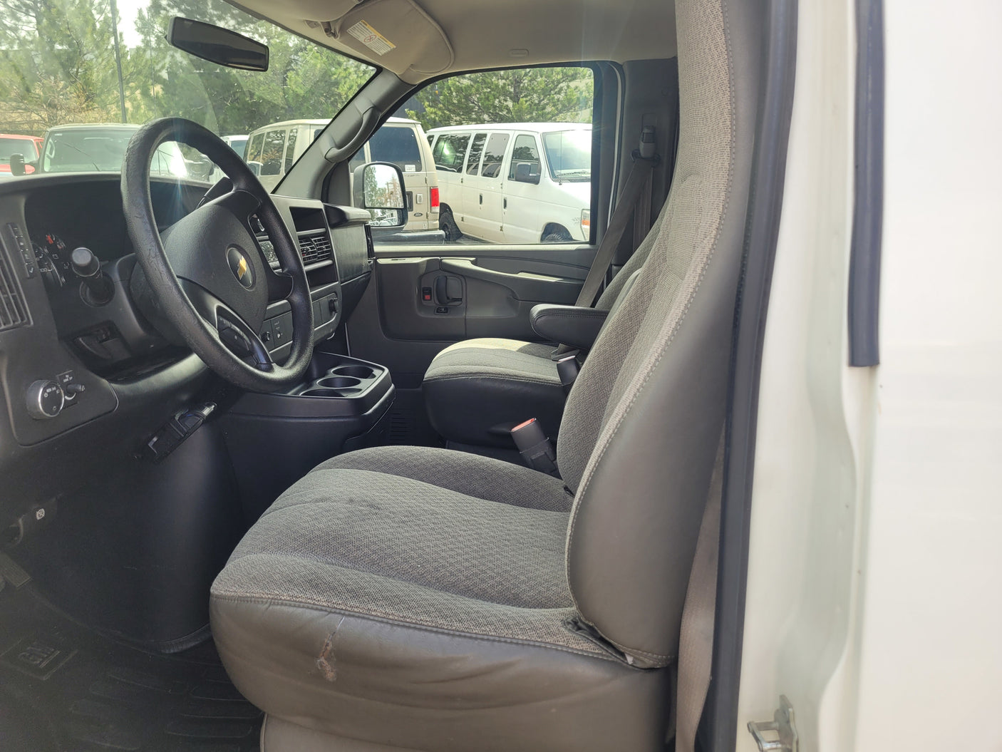 Driver's cockpit of a work van, possibly for rv rental. Shows steering wheel, dashboard, and front seats with wear.