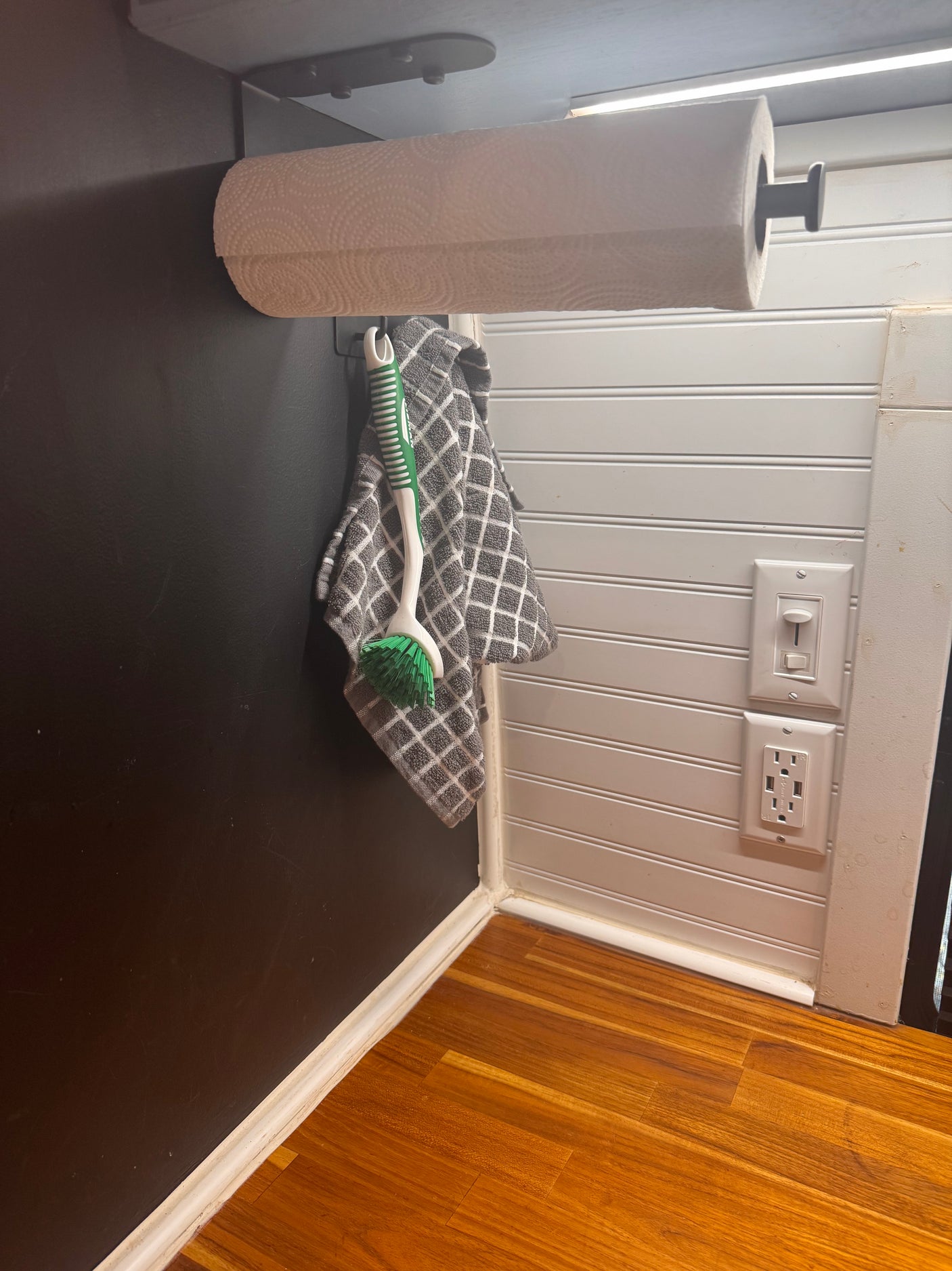 RV rental detail: convenient paper towel roll, hanging brush, and modern outlets, set against contrasting walls & wood floor.
