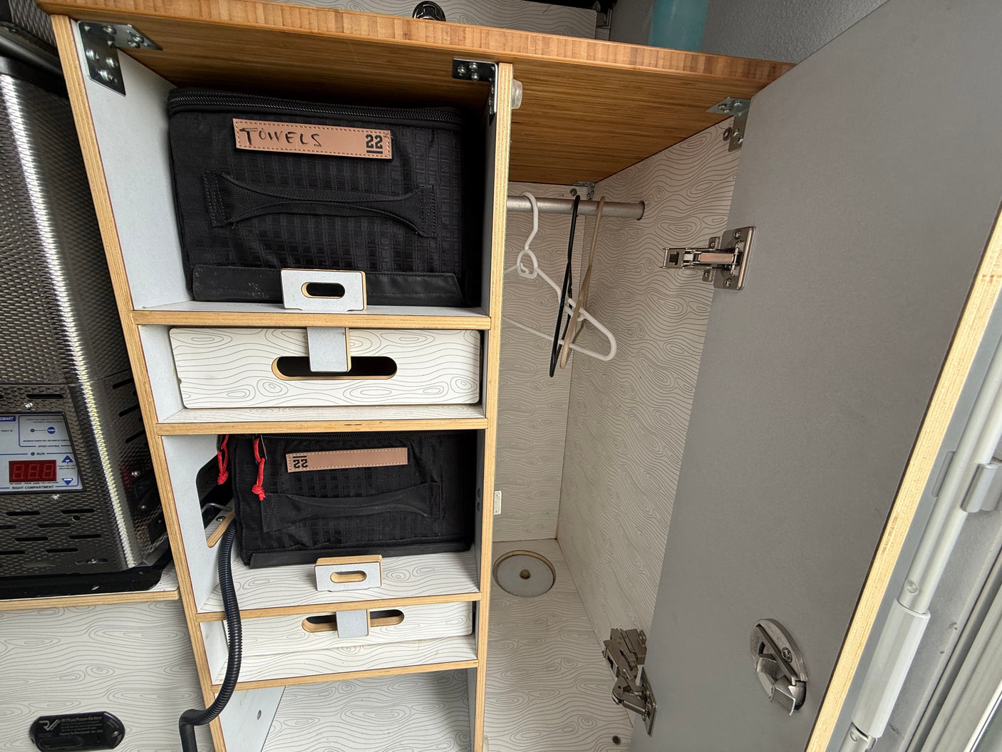 RV rental's organized storage: wooden cabinet with labeled bags, patterned drawers, a hanging rod, and a utility appliance.