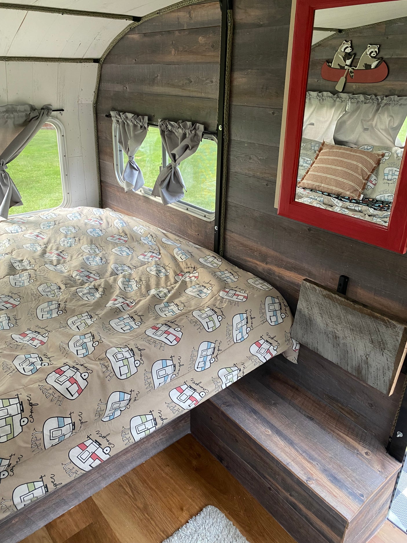 Cozy RV rental interior showcasing a bed with "Happy Camper" bedding, wood paneling, and a mirror.
