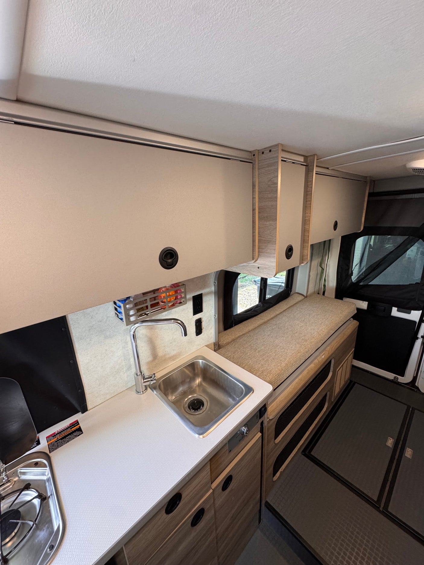 Inside an rv rental: functional kitchenette with sink, stove, storage cabinets, and comfy bench seating.