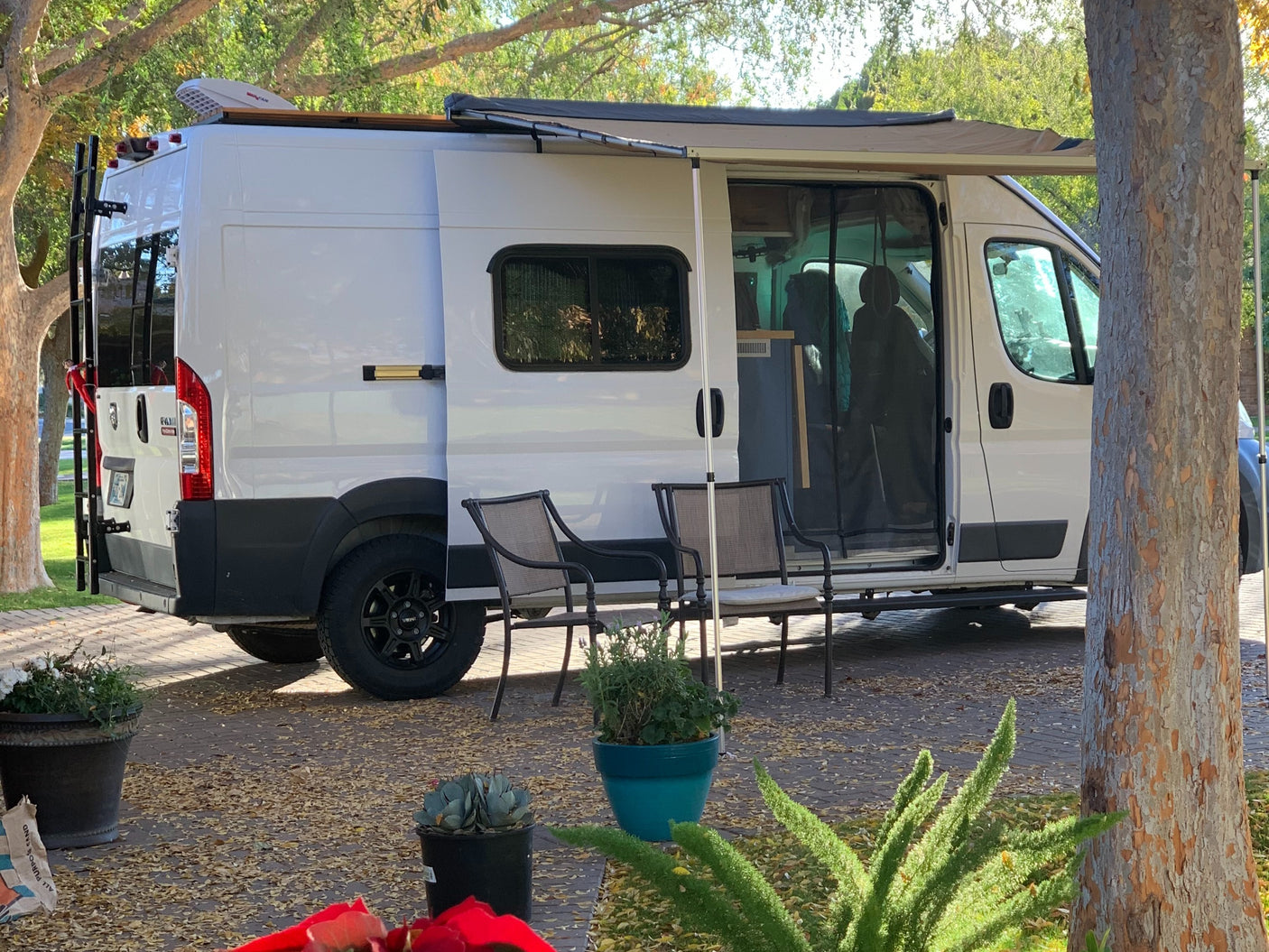 RV rental: White camper van with an extended awning, chairs, and potted plants creates a cozy outdoor living space.