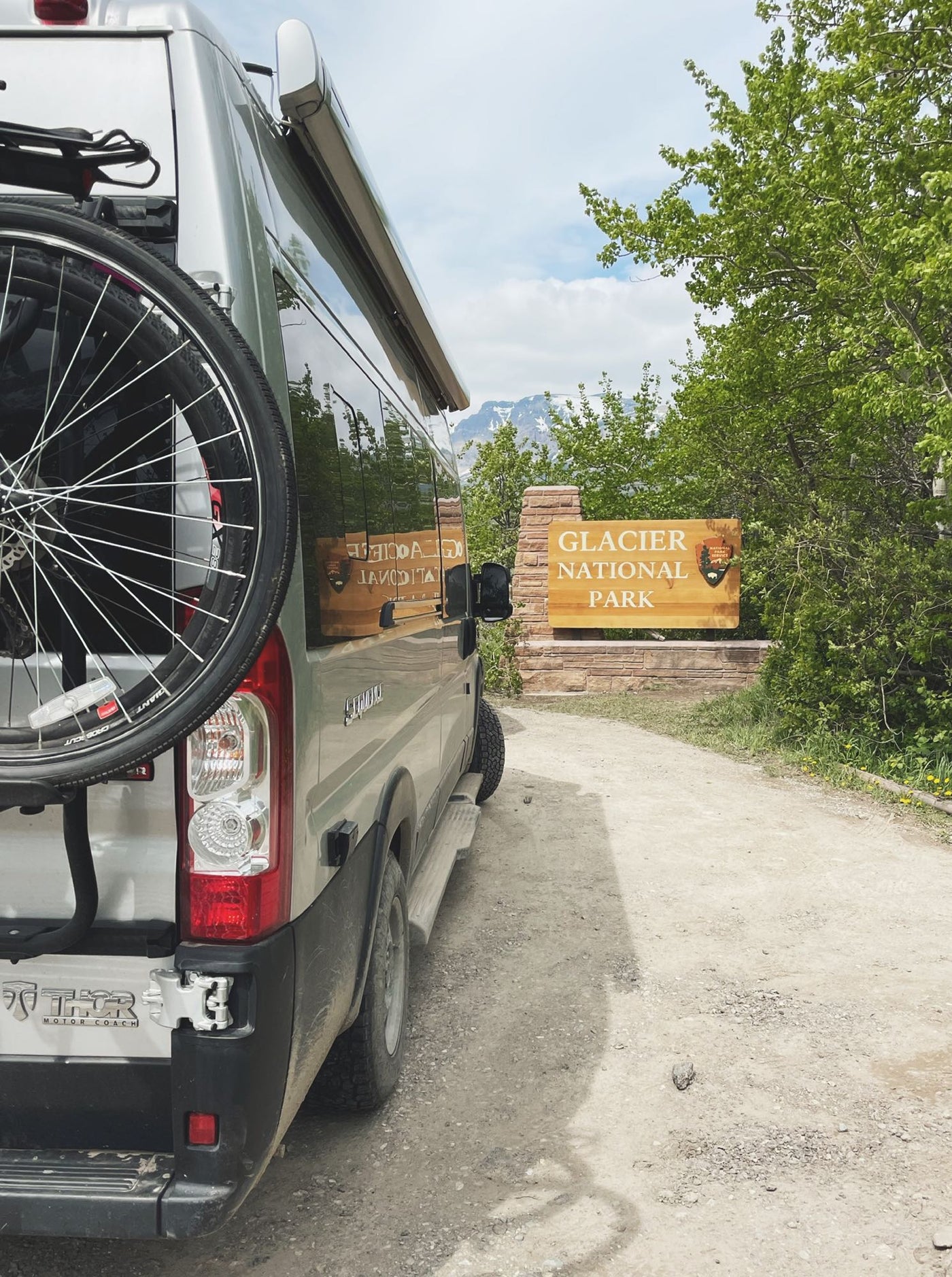 ready for a road trip adventure.|An RV rental with bike rack at Glacier National Park's entrance on a dirt road — photo 1