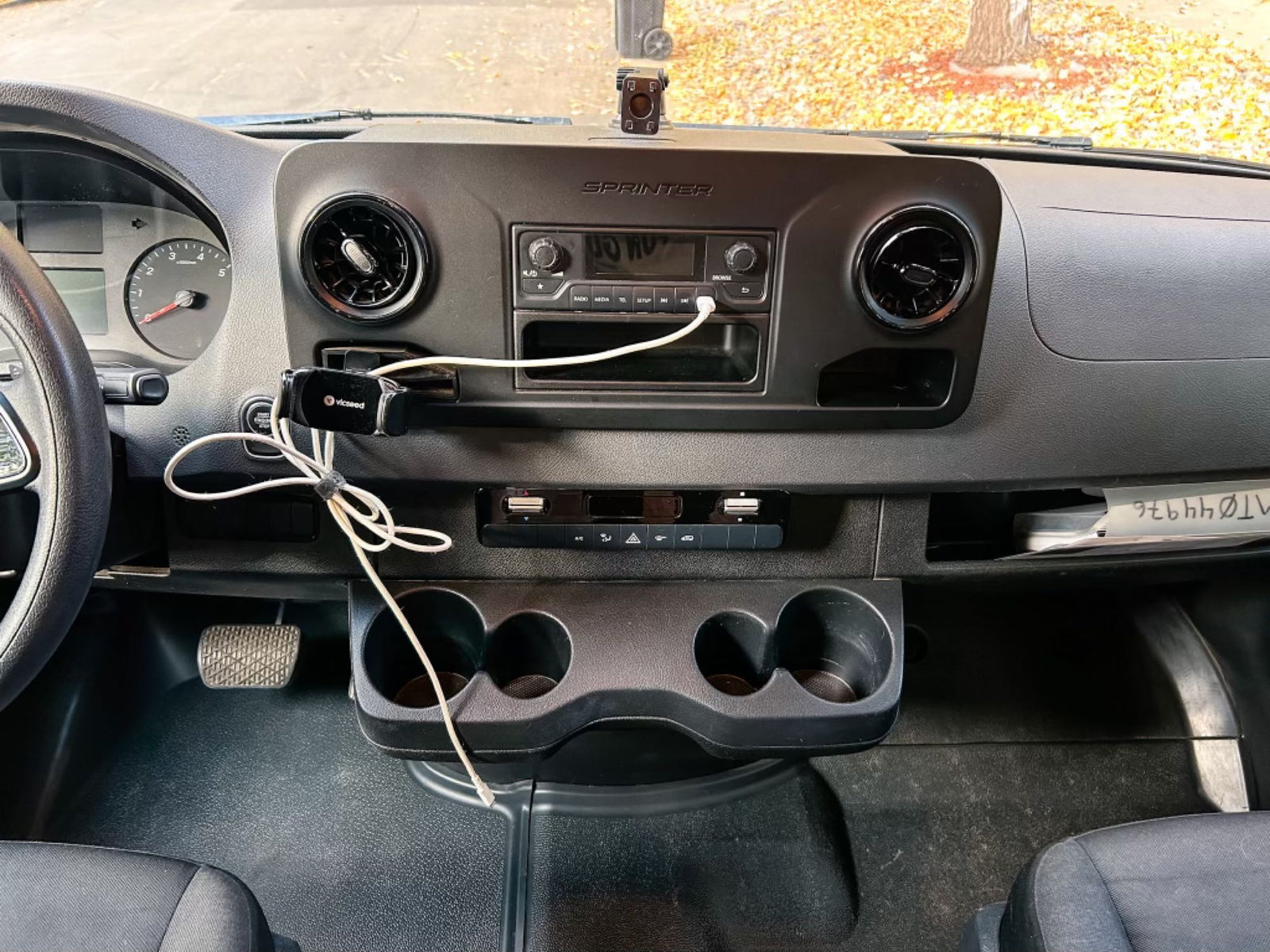 Inside an rv rental Sprinter van, this photo shows the dashboard, steering wheel, radio, cupholders, and driver's footwell.