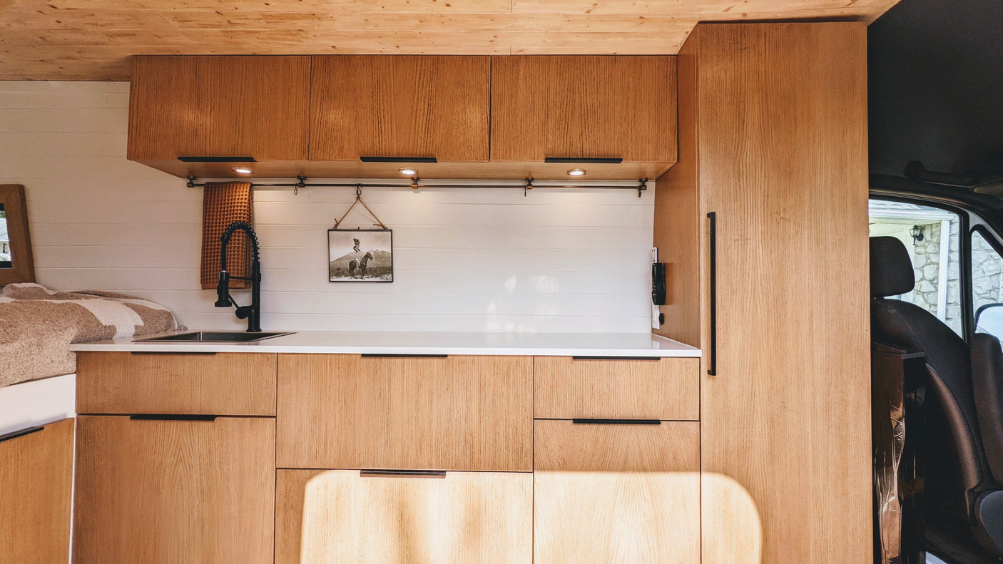 This RV rental showcases a bright, modern interior with natural wood cabinets, a compact kitchen sink, and cozy bed area.