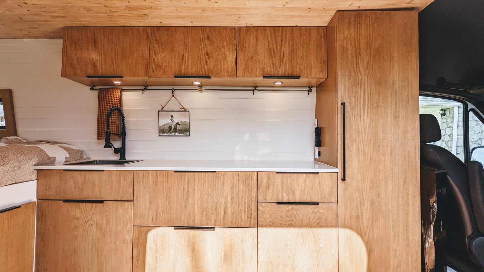 This RV rental showcases a bright, modern interior with natural wood cabinets, a compact kitchen sink, and cozy bed area.