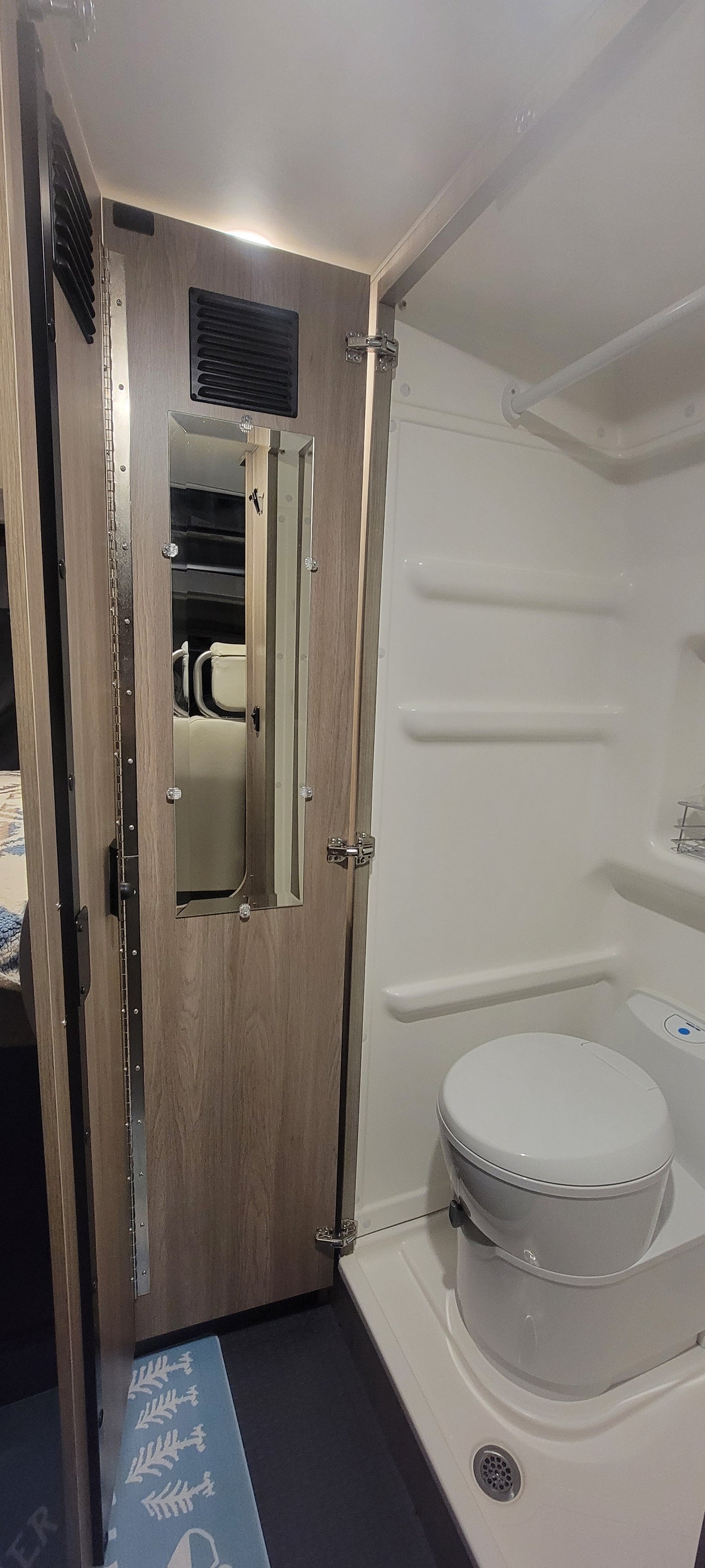 RV rental wet bath: Features toilet, shower, mirror, vent, and light, set in wood-look paneling.