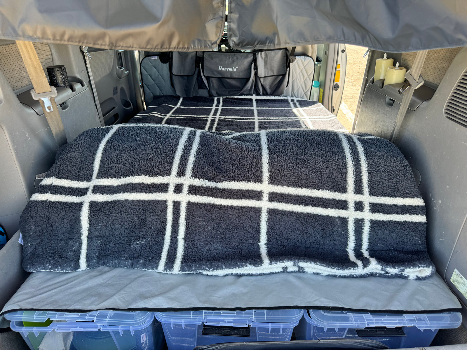 This RV rental interior features a cozy bed with a plaid blanket, storage bins, and Hanemia hanging organizers.