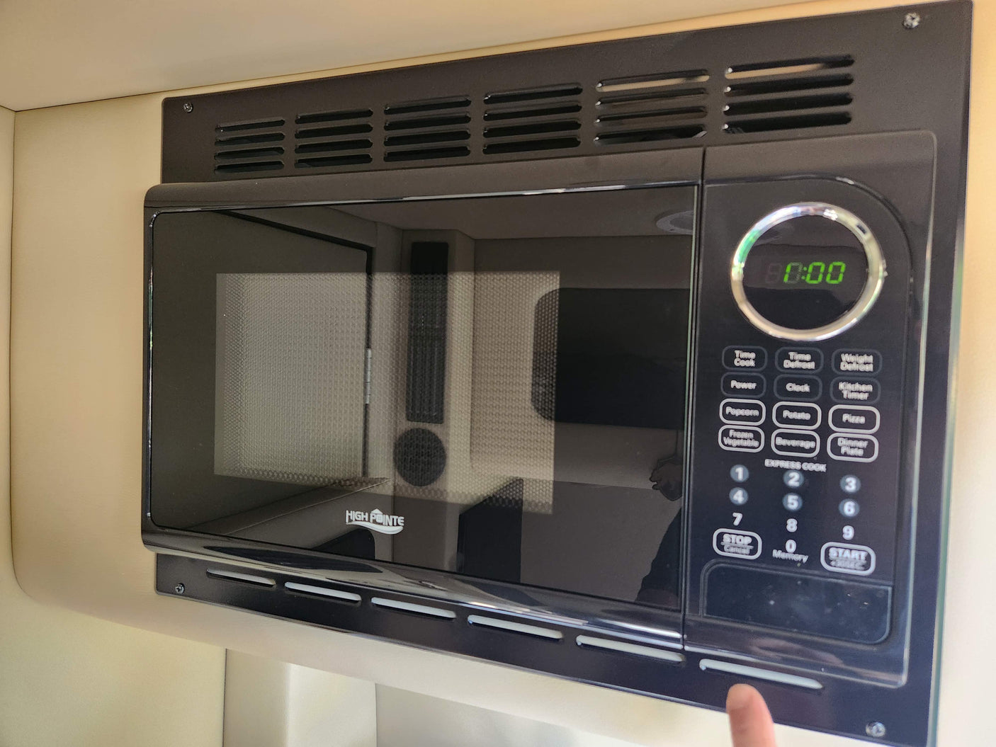 Black High Pointe microwave, built into an RV rental. Features a digital clock and multiple cooking options for travel convenience.
