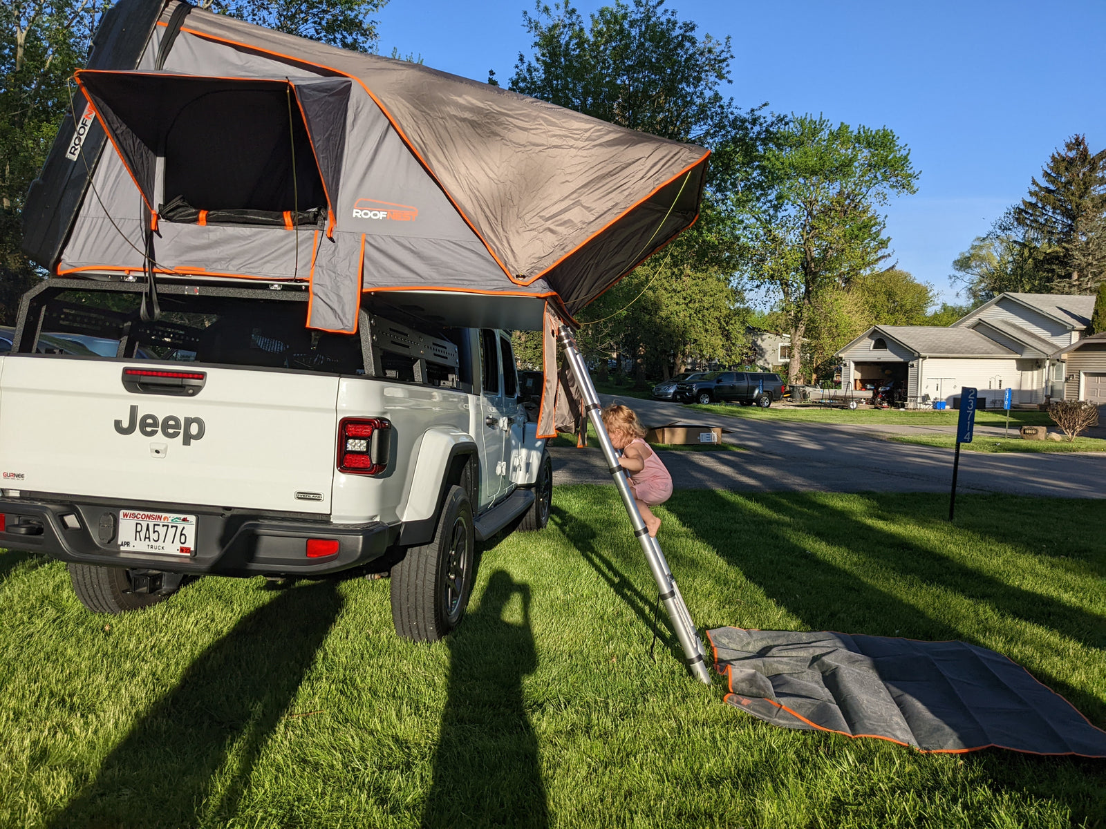 perfect for outdoor adventures or a unique RV rental alternative.|A happy toddler peeks from a grey rooftop tent mounted on a vehicle